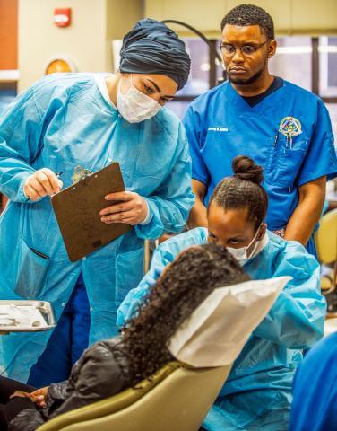 Nurses looking on and taking notes as a doctor examines a patient 